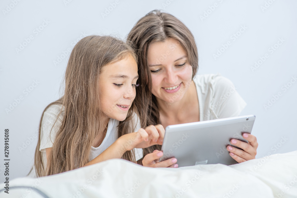 Happy loving family. Beautiful young woman and her little daughter are using a digital tablet and smiling while lying in bed at home Happy loving family. Beautiful young woman and her little daughter are using a digital tablet and smiling while lying in bed at home