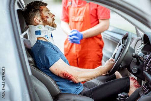 Injured man with deep wounds and corset on his neck sitting on the driver seat during the medical assistance after the accident