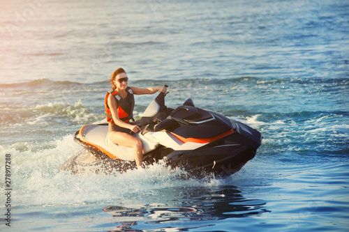 Young adult sporty caucasian woman riding jet ski in ocean blue water at warm evening sunset. Beach extreme sport activities and recreation