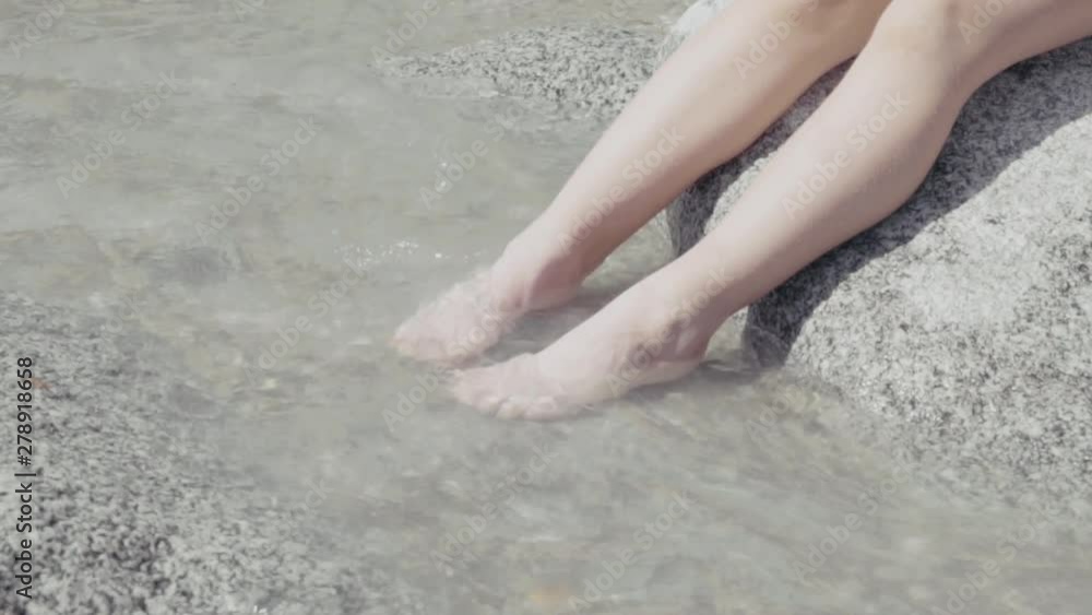 Close-up of a little girl sitting on a stone and dipping her legs and feet in on stream on a sunny day in the Italian Alps Close-up of a little girl sitting on a stone and dipping her legs and feet in on stream on a sunny day in the Italian Alps