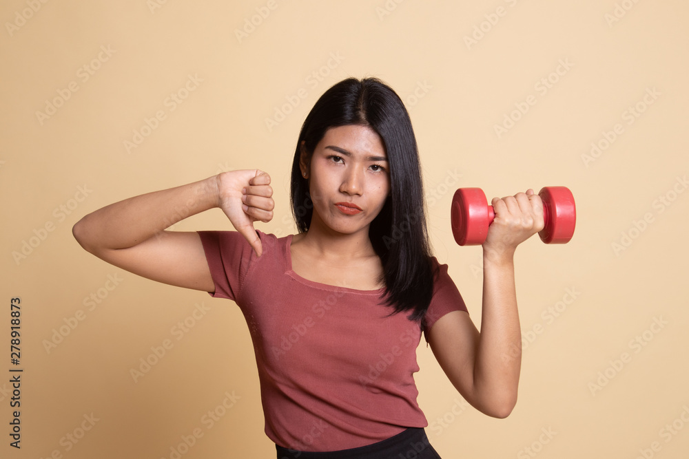 Unhappy Asian woman thumbs down with dumbbells. Unhappy Asian woman thumbs down with dumbbells.