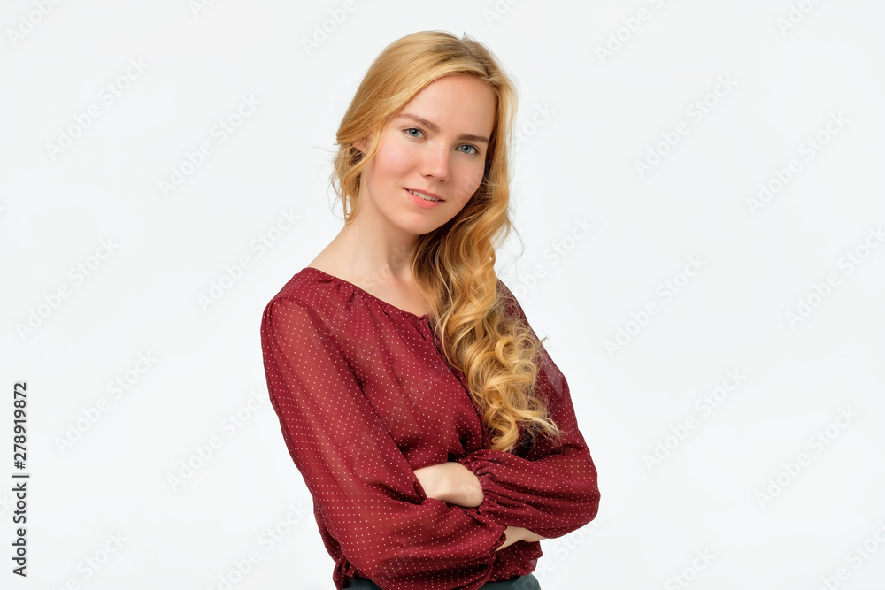 Charming caucasian female with blonde hair in red shirt gently looking at camera, smiling while listening to good news. Positive facial human emotion. Studio shot Charming caucasian female with blonde hair in red shirt gently looking at camera, smiling while listening to good news. Positive facial human emotion. Studio shot