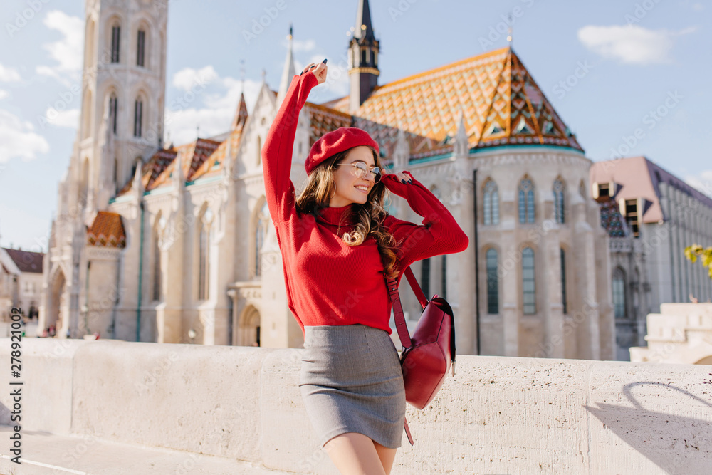 Naklejka premium Winsome girl in gray skirt dancing with happy face expression with palace on background. Outdoor portrait of lovely lady posing in front of old beautiful building.