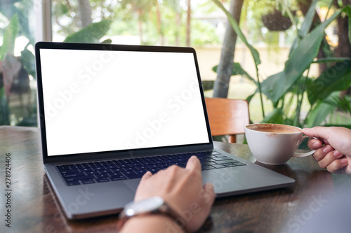 Mockup image of a woman using and touching laptop touchpad with blank white desktop screen while drinking coffee