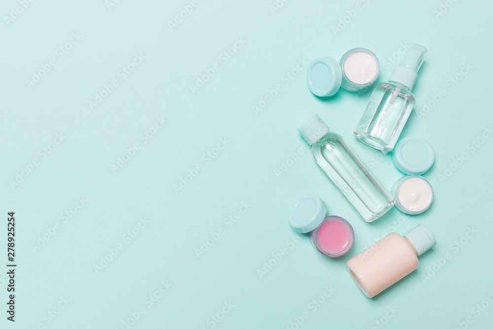 Top view composition of small travelling bottles and jars for cosmetic products on blue background. Facial skin care concept with copy space for your design