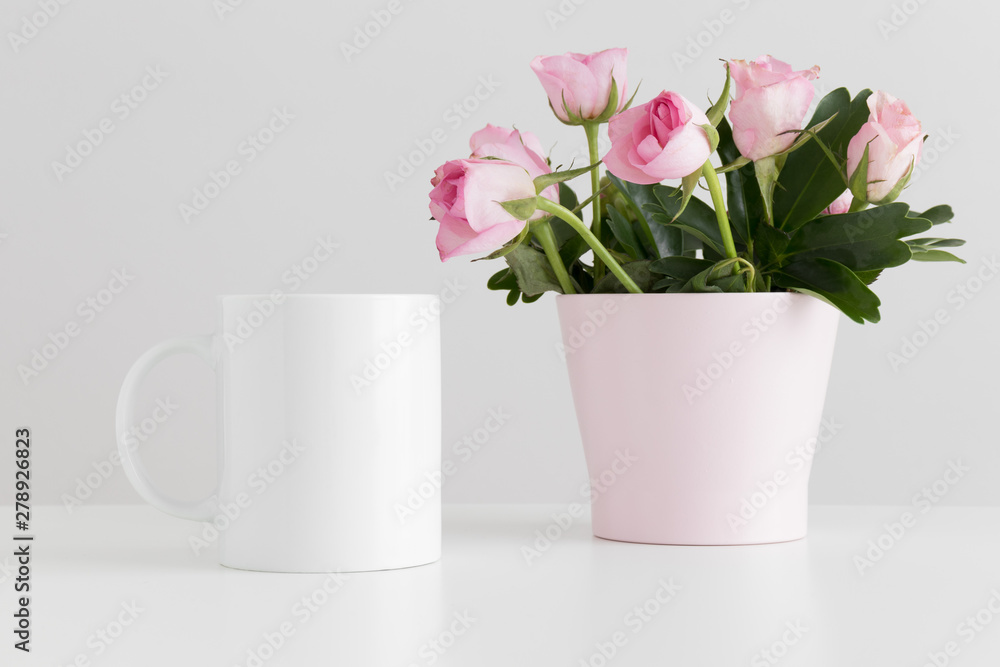 Mug mockup with pink roses in a pot on a white table.