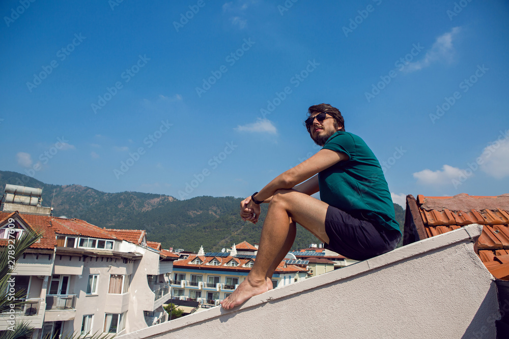 man in the green t-shirt shorts and sunglasses sitting on the roof