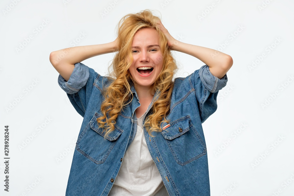 Beautiful young woman in denim jeans is holding head in hands, shouting. She is told great news about her tests results. Studio shot. Beautiful young woman in denim jeans is holding head in hands, shouting. She is told great news about her tests results. Studio shot.