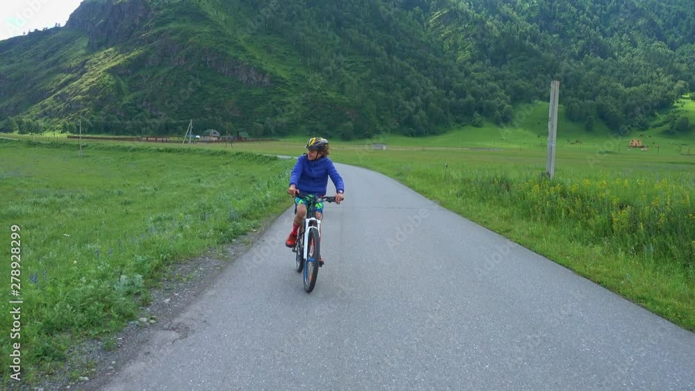 Happy boys riding bikes on road in mountains, cows grazing in the meadow near, Altai Republic, Russia. Happy boys riding bikes on road in mountains, cows grazing in the meadow near, Altai Republic, Russia.