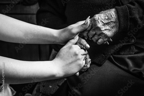 girl holds her old grandmother for her hand in black and white . help and support for the elderly. daughter and mother.