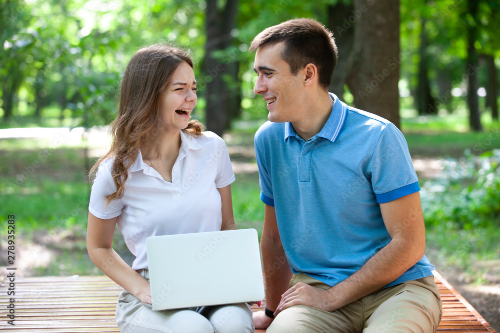 Young couple sitting together on bench in park and using laptop Young couple sitting together on bench in park and using laptop