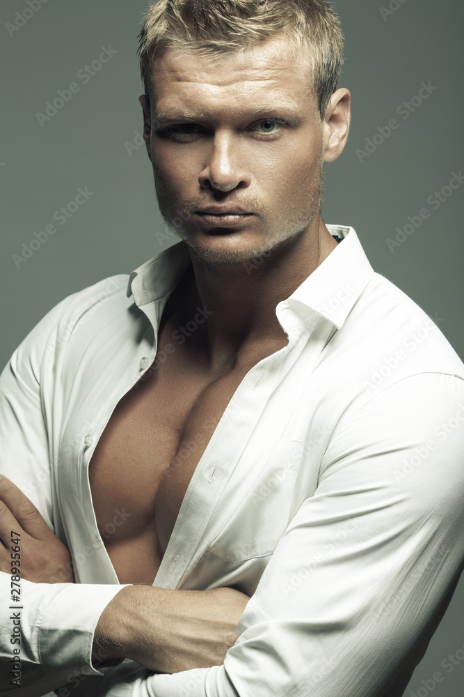 Male fashion, beauty concept. Portrait of brutal young man with short wet  blond hair wearing white shirt, posing over gray background. Classic style.  Close up. Hands crossed. Studio shot Stock Photo |