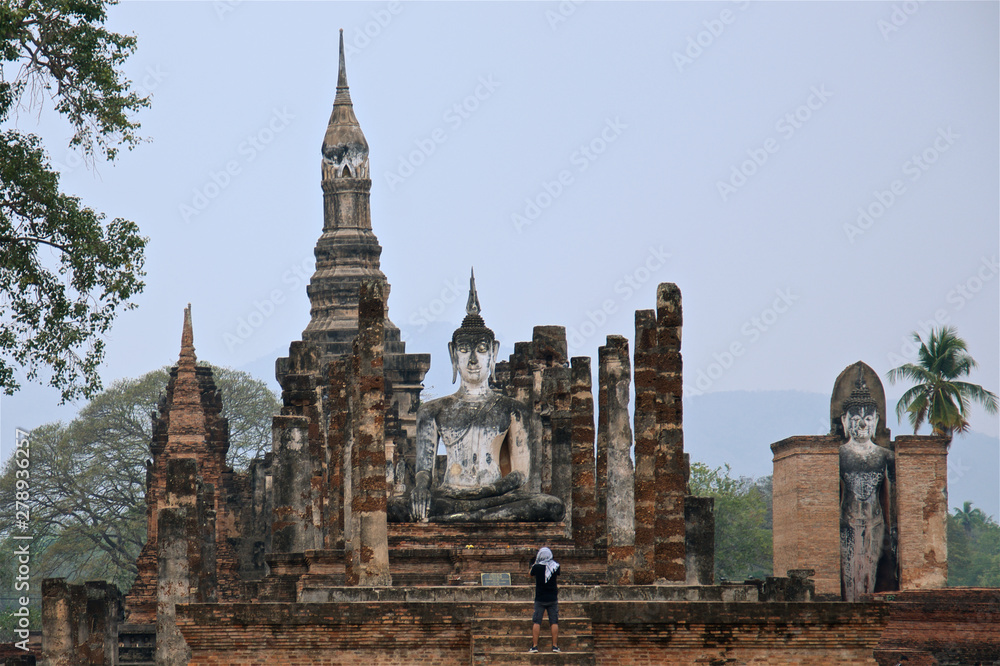 male tourist in east headscarf is looking on big budda statue famous Sukhothai Historical Park, a UNESCO World Heritage Site, Foggy spring day in the ancient capital of Sukhothai. Thailand