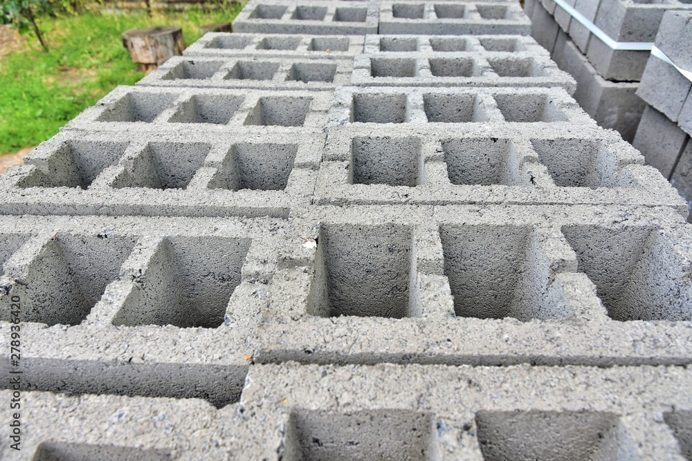 Stack of gray textured cinder blocks for house or fence building. Construction Materials. Pallet with cinderblocks and pile of sand on background. Row of grey concrete bricks. Brickwork 
