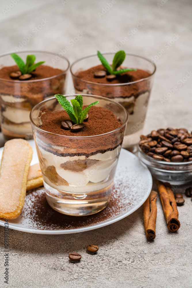 Classic tiramisu dessert in a glass cup and savoiardi cookies on plate on concrete background Classic tiramisu dessert in a glass cup and savoiardi cookies on plate on concrete background