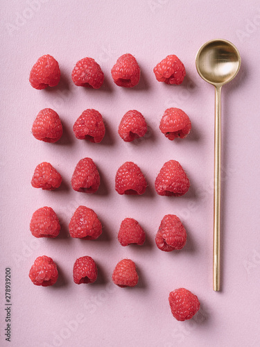 Raspberry lined up with golden spoon on pink background photo