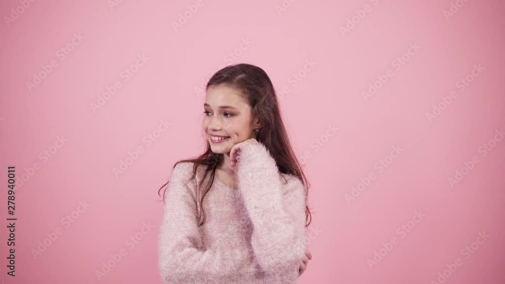 Studio portrait of lovely long brown haired teen girl expressing joy, looking on sides then smiling to the camera. Pink background. Concept of emotions Studio portrait of lovely long brown haired teen girl expressing joy, looking on sides then smiling to the camera. Pink background. Concept of emotions
