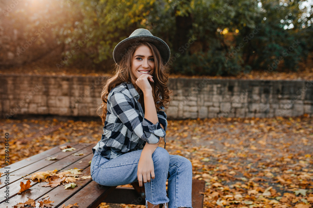 Spectacular brown-haired girl in casual clothes relaxing in park in good autumn weather. Refined white lady in gray elegant hat posing in sunny morning in yard, covered with fallen leaves. Spectacular brown-haired girl in casual clothes relaxing in park in good autumn weather. Refined white lady in gray elegant hat posing in sunny morning in yard, covered with fallen leaves.