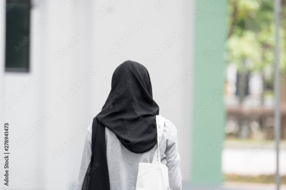 Female muslim girl back view walking. Female muslim black hijab and white shirt