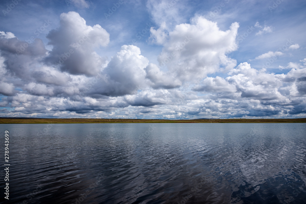 panoramic view of the blue sky with white fluffy clouds reflecting on the mirror-like surface of the water of an amazing lake