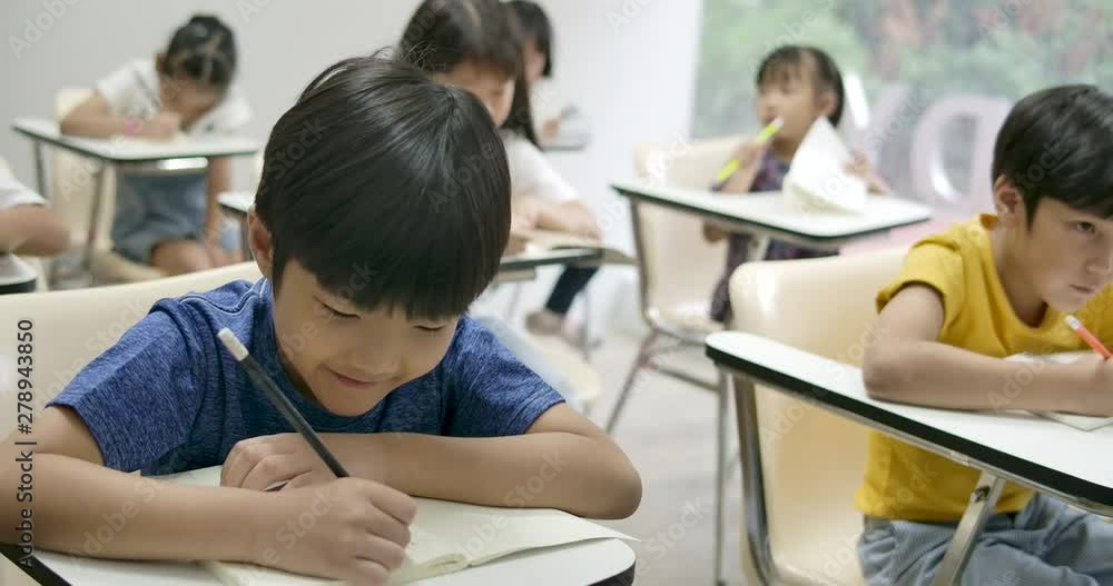 School boy writing on his notebook, taking exam in the classroom. School boy writing on his notebook, taking exam in the classroom.
