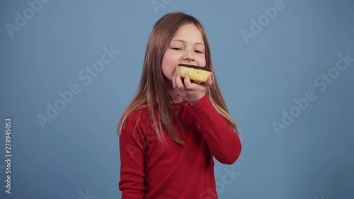 Little girl in red sweater is eating a chocolate donut on a colored background. Enjoying the taste. Child 7-10 years old, fair hair. Shooting in the studio. Food concept photo