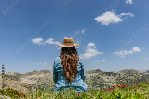 Frau mit Stohhut sitzt zwischen Alpenrosen