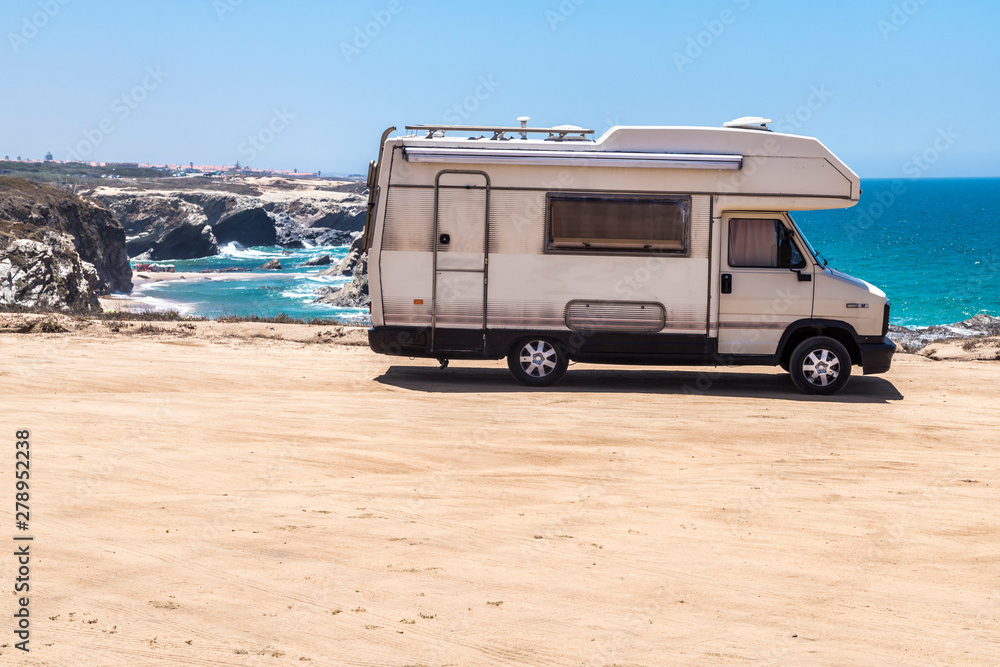 Una autocaravana aparcada en la costa portuguesa,  con la playa de Porto Covo al fondo