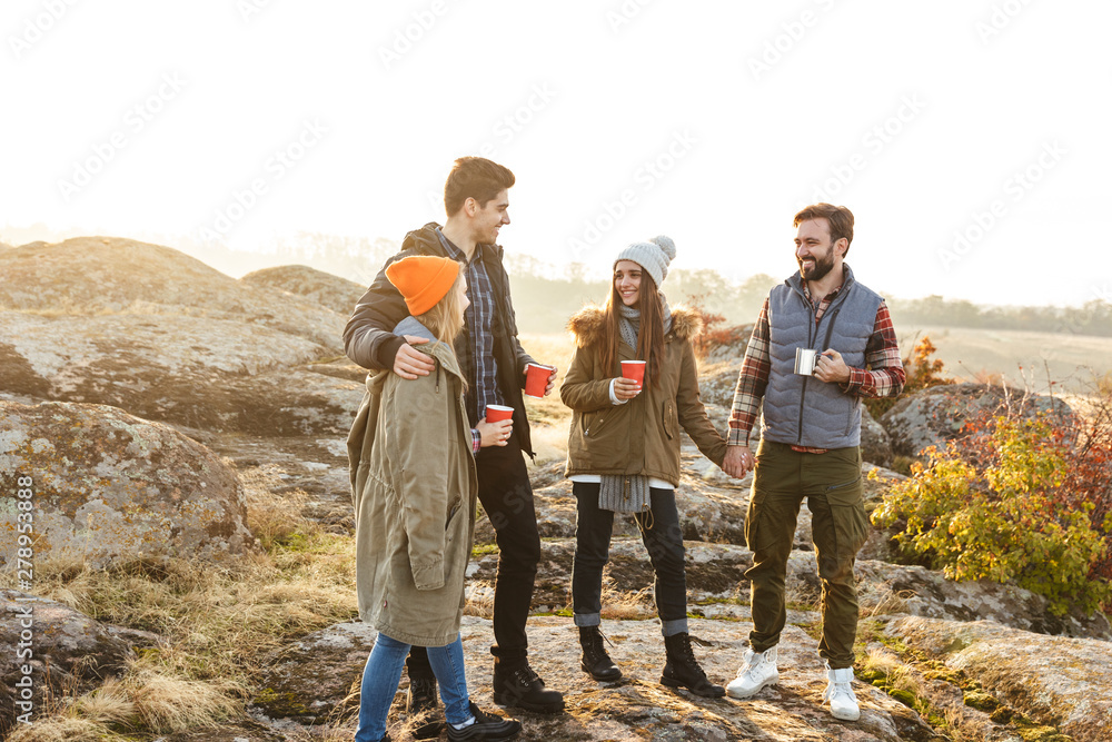 Group of friends outside in free alternative vacation camping over mountains drinking hot tea talking with each other.
