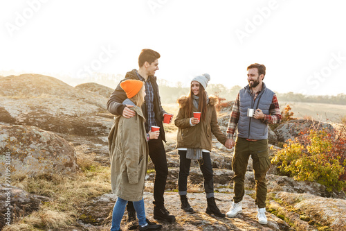 Group of friends outside in free alternative vacation camping over mountains drinking hot tea talking with each other.