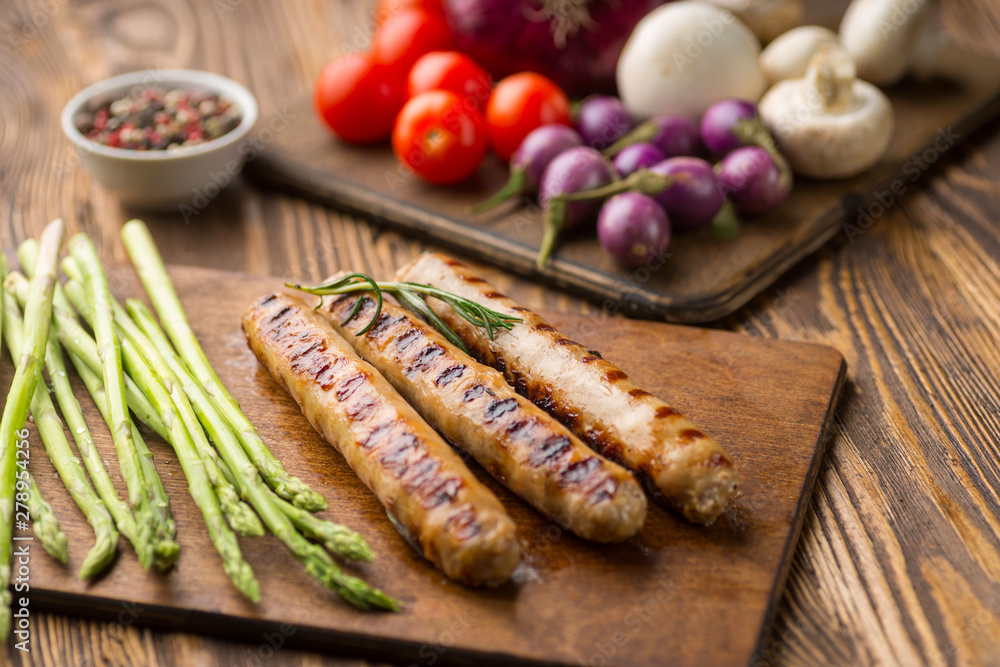 Sausages with vegetables on wooden background.