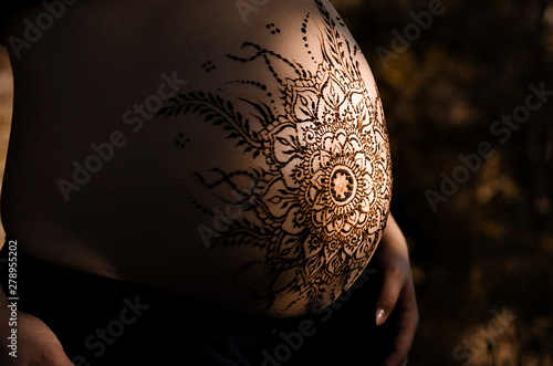 Pregnant belly with mehndi henna tattoo design, low key lighting