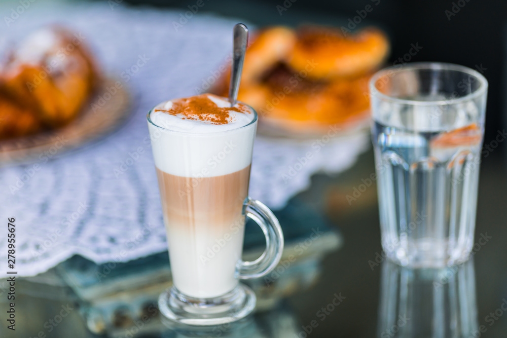Coffee latte in glass with milk foam and cocoa, cinnamon powder and cake bisquit for breakfast Coffee latte in glass with milk foam and cocoa, cinnamon powder and cake bisquit for breakfast