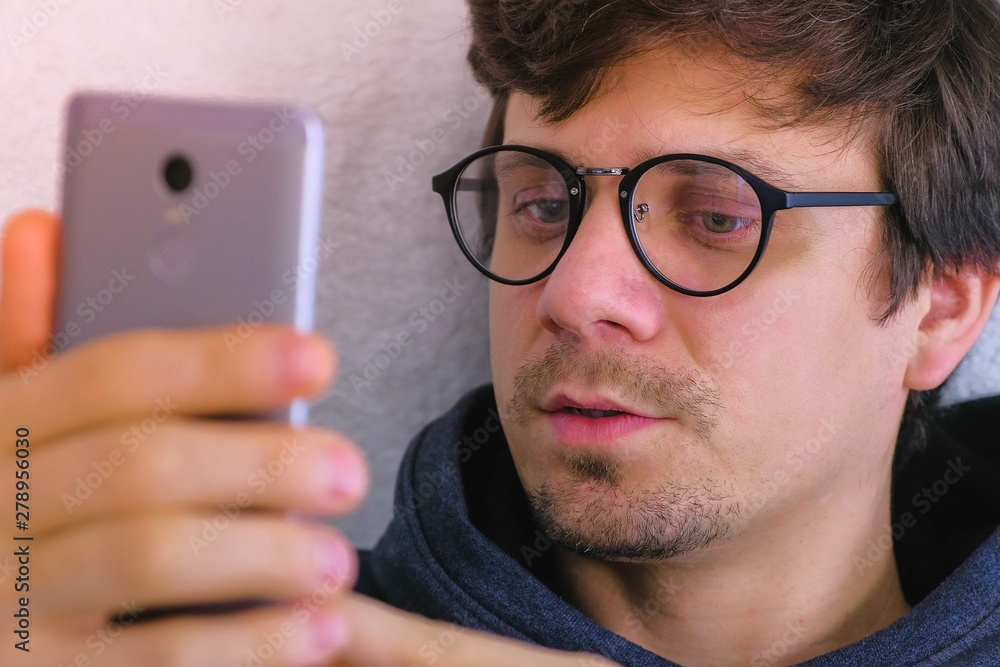 Happy young man in glasses speaking video chat on smartphone sitting in armchair, online date, face close-up