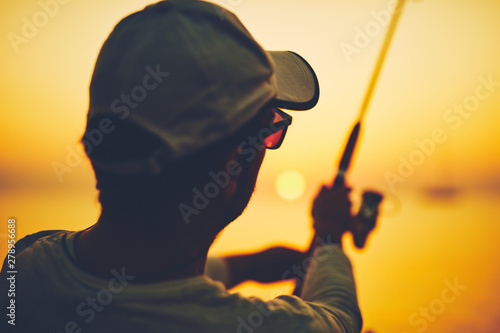 Silhouette of a fisherman fishing in sunset time on the open sea. © astrosystem