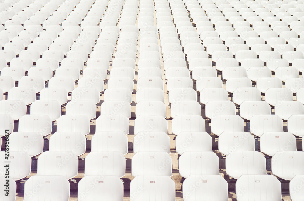 Fototapeta premium Rows of empty white plastic seats at the tribune in an open sports stadium