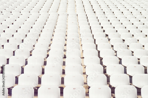 Rows of empty white plastic seats at the tribune in an open sports stadium photo