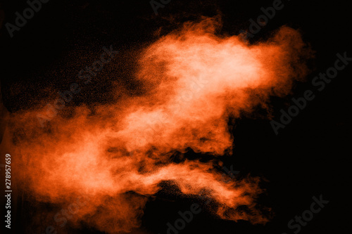 Freeze motion of orange powder exploding on black background. Abstract design of color dust cloud. Particles explosion.