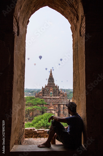 A young man sitting in a temple at the lovely sunrise with balloons on top of the temples in Bagan, Myanmar.