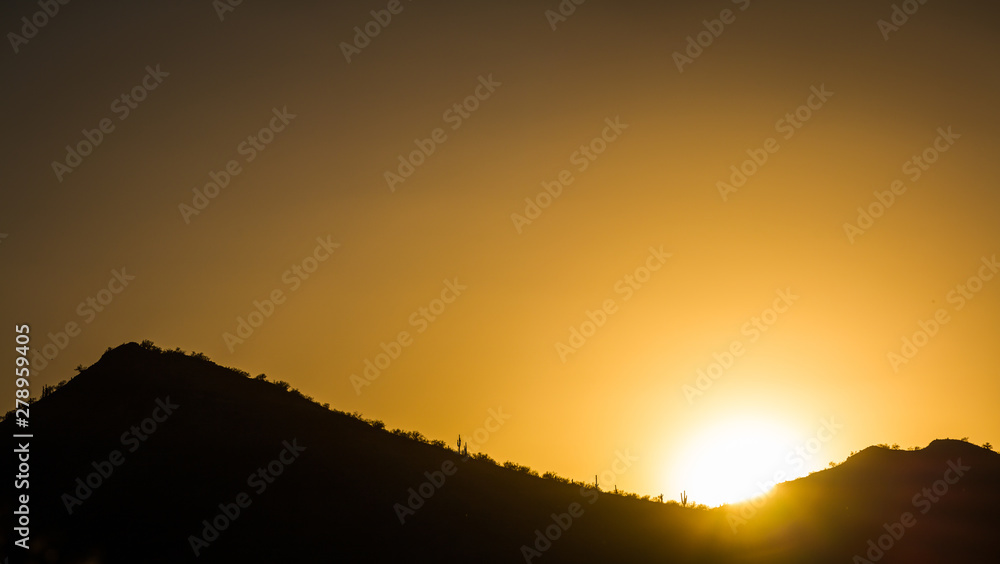 The sun setting behind a mountain in the Sonoran Desert of Arizona, filling the sky with golden light. The sun setting behind a mountain in the Sonoran Desert of Arizona, filling the sky with golden light.