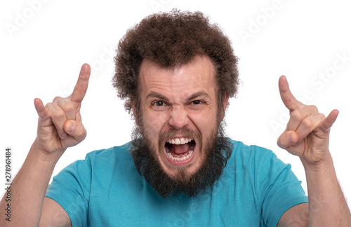 Crazy bearded happy Man with funny Curly Hair making rock and roll gesture, isolated on white background. Portrait of Cheerful guy screaming and looking at camera - studio shot.