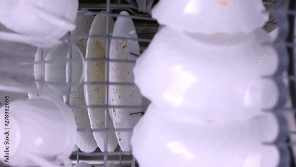 Man's hand puts a white dirty cup in the upper basket of dishwasher and pushes it with kitchenware. Top view, close-up hand. Man's hand puts a white dirty cup in the upper basket of dishwasher and pushes it with kitchenware. Top view, close-up hand.