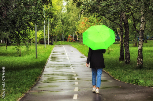 Young beautiful girl walking alone under green umbrella in the city park in summertime