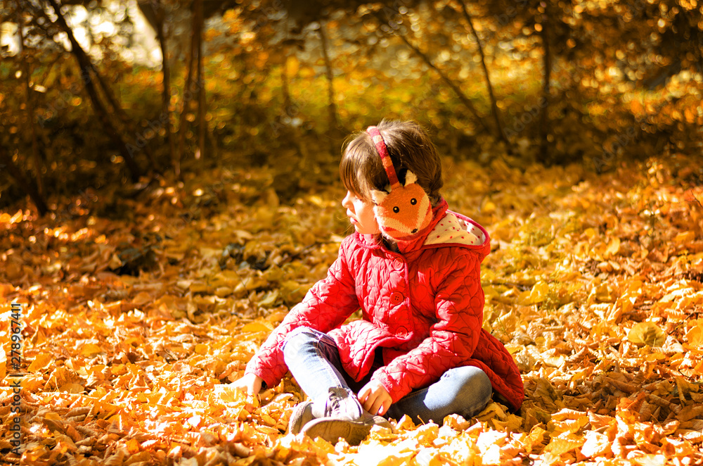 Beautiful little girl in red jacket is sitting on yellow leaves and playing on warm and sunny autumn day. Happy childhood concept Beautiful little girl in red jacket is sitting on yellow leaves and playing on warm and sunny autumn day. Happy childhood concept