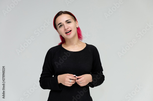 Portrait to the waist of a pretty girl with red hair on a white background in a black jacket. Standing right in front of the camera in a studio with emotions, talking, showing hands, smiling