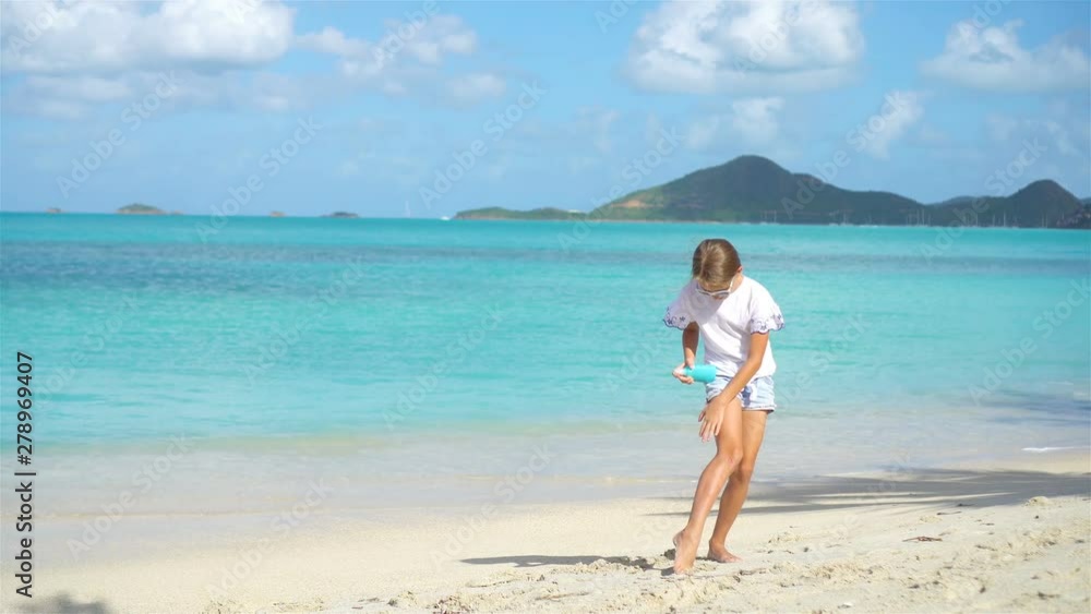 Little girl with bottle of sun cream sitting at tropical beach Little girl with bottle of sun cream sitting at tropical beach