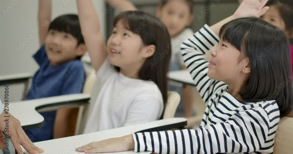 Group of joyful asian elementary students raising their arms to answer a question from teacher at classroom. Kindergarten pre school concept. Group of joyful asian elementary students raising their arms to answer a question from teacher at classroom. Kindergarten pre school concept.