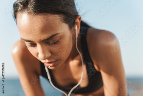 Serious beautiful young strong sports woman outdoors at the beach at morning have a rest listening music with earphones.