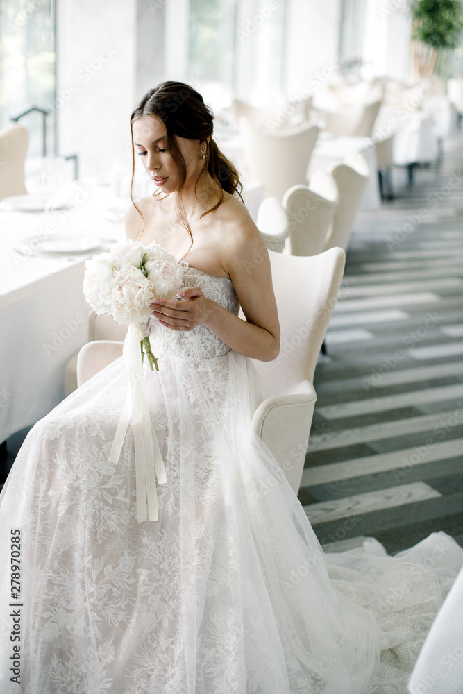beautiful bride with a bouquet in hand, sits in a restaurant beautiful bride with a bouquet in hand, sits in a restaurant