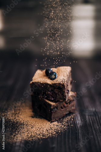 brownie cake sprinkled with ground cocoa on a dark background